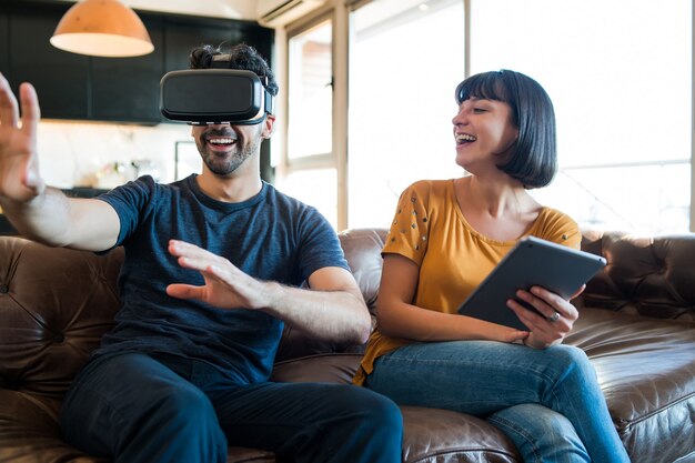 Retrato de um jovem casal se divertindo juntos e jogando videogame com óculos de realidade virtual enquanto fica em casa