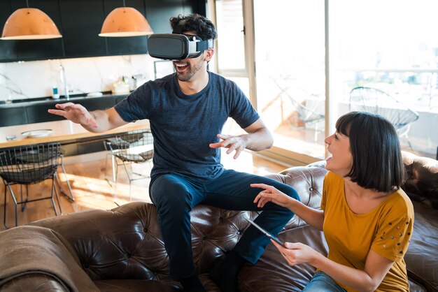 Retrato de um jovem casal se divertindo juntos e jogando videogame com óculos de realidade virtual enquanto fica em casa