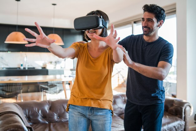 Retrato de um jovem casal se divertindo juntos e jogando videogame com óculos de realidade virtual enquanto fica em casa