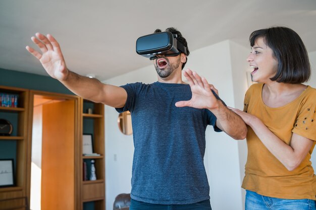 Retrato de um jovem casal se divertindo juntos e jogando videogame com óculos de realidade virtual enquanto fica em casa