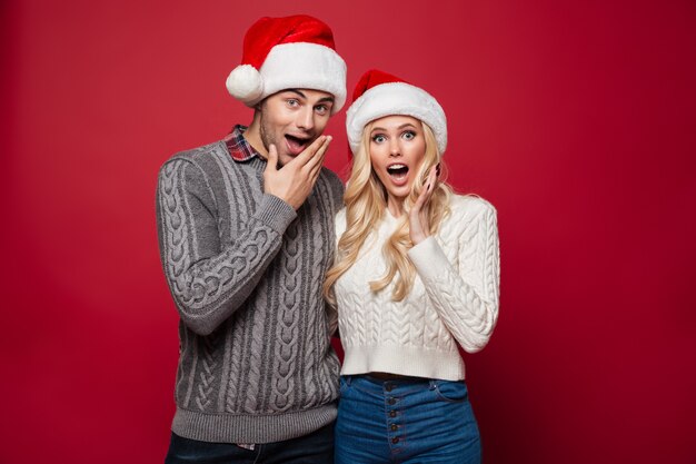 Retrato de um jovem casal surpreso em chapéus de natal