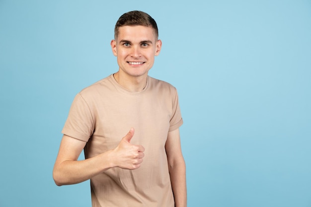 Retrato de um jovem caucasiano posando isolado sobre o fundo azul do estúdio com copyspace para anúncio Conceito de emoções humanas