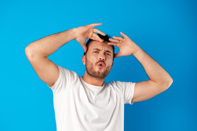 Retrato de um jovem confuso de mãos dadas na cabeça sobre um fundo azul