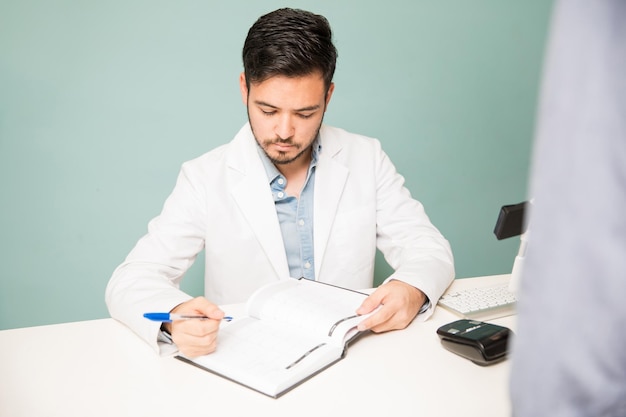 Retrato de um jovem de jaleco marcando uma consulta para um cliente na recepção de um spa