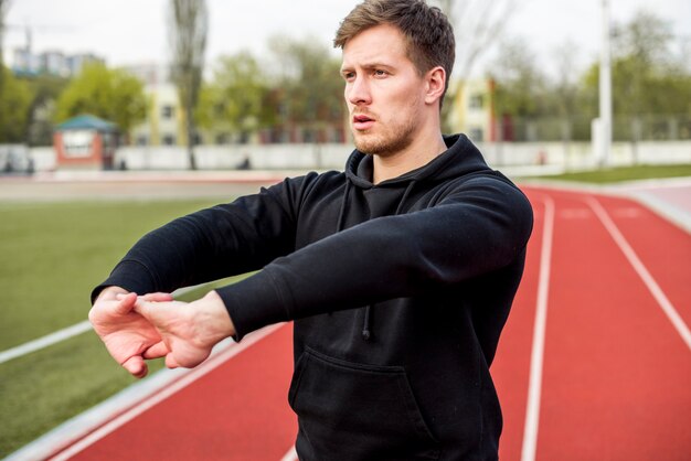 Retrato de um jovem de pé na pista de corrida, esticando a mão