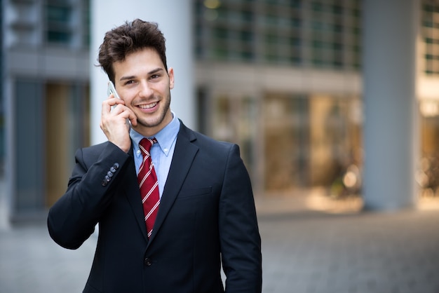 Retrato de um jovem empresário falando ao telefone ao ar livre em frente ao seu escritório