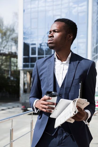 Retrato de um jovem empresário segurando o tablet digital; jornal e copo de café descartável