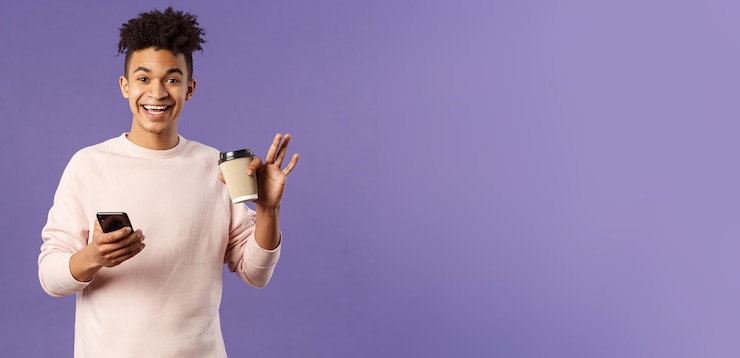 Foto grátis retrato de um jovem estudante masculino alegre com uma xícara de café e celular acenando com a mão para dizer oi sm