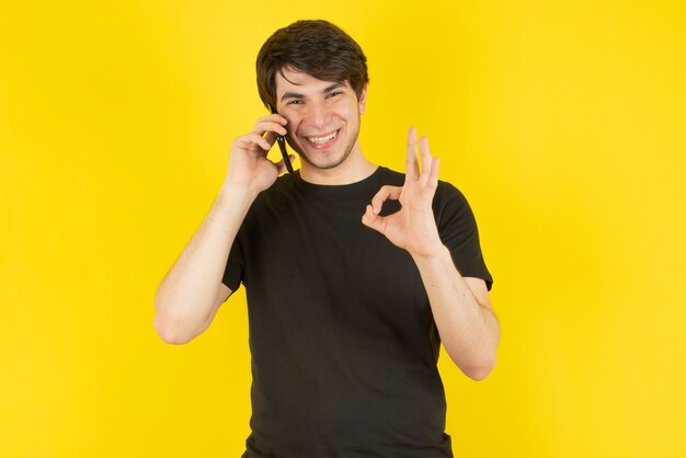 Retrato de um jovem falando no celular contra amarelo.