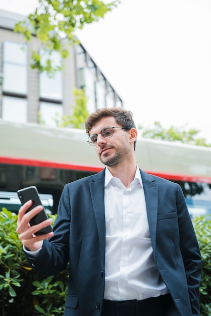 Retrato, de, um, jovem, homem negócios fica, frente, predios, usando, telefone móvel