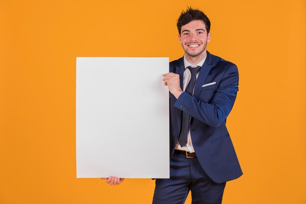 Retrato, de, um, jovem, homem negócios, segurando, branca, em branco, painél publicitário, contra, um, laranja, fundo