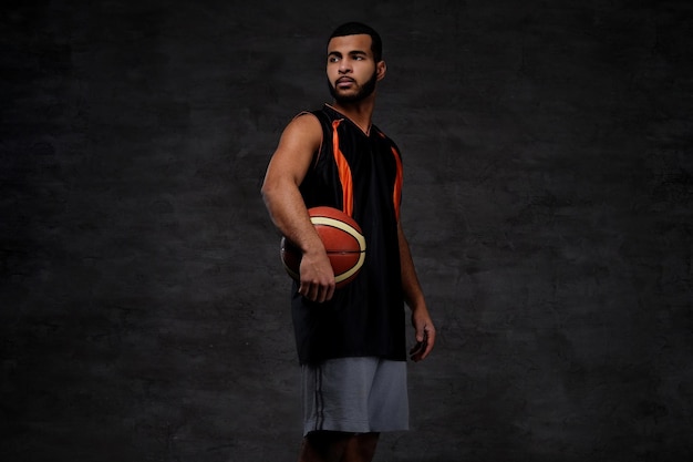 Retrato de um jovem jogador de basquete afro-americano em sportswear isolado sobre fundo escuro.