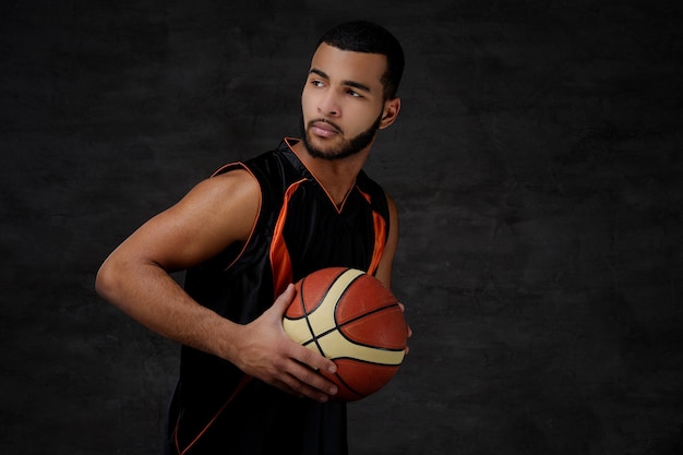 Retrato de um jovem jogador de basquete afro-americano em sportswear isolado sobre fundo escuro.