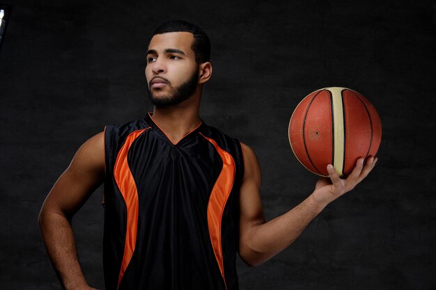 Retrato de um jovem jogador de basquete afro-americano em sportswear isolado sobre fundo escuro.