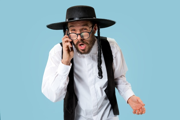 Retrato de um jovem judeu ortodoxo com telefone celular no estúdio. Purim, negócios, empresário, festival, feriado, celebração, judaísmo, conceito de religião.
