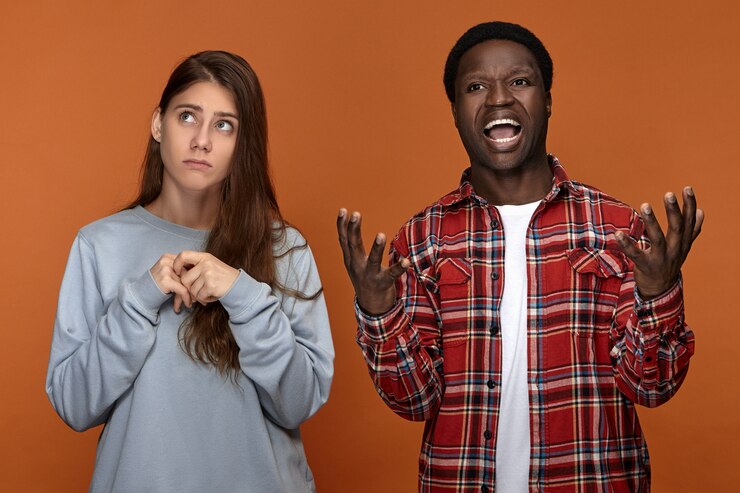 Foto grátis retrato de um jovem marido de pele escura irritado, gesticulando emocionalmente e gritando, ficando com raiva de sua esposa caucasiana que não consegue tomar uma decisão ou escolha, olhando para cima com uma expressão incerta