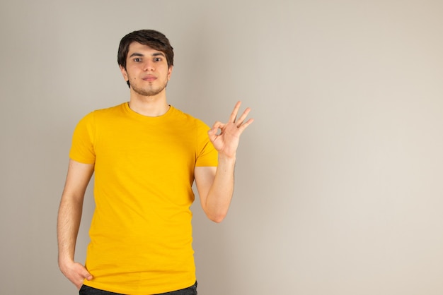 Retrato de um jovem mostrando gesto ok contra cinza.