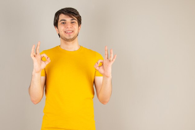 Retrato de um jovem mostrando gesto ok contra cinza.