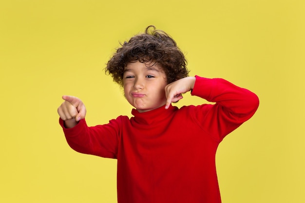 Retrato de um jovem rapaz encaracolado com roupa vermelha em fundo amarelo studio. Infância, expressão, educação, conceito divertido.