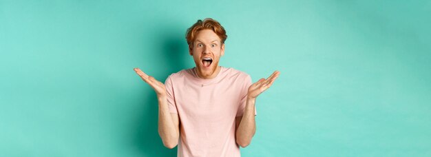 Retrato de um jovem surpreso e feliz com cabelos ruivos espalhando as mãos para o lado e ofegante de admiração