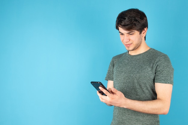 Retrato de um jovem usando um telefone celular contra o azul.