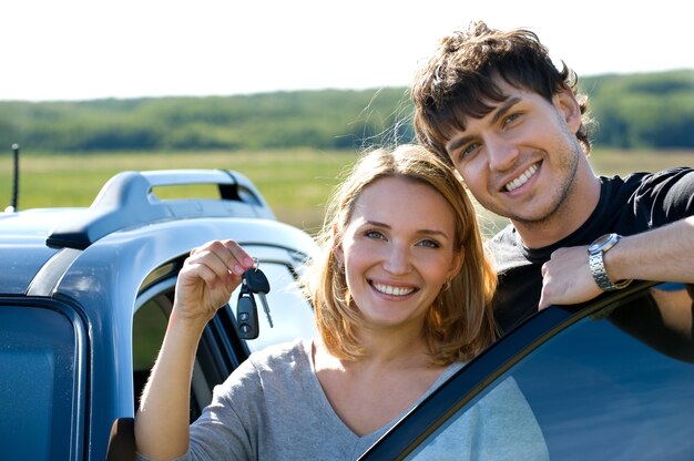 Retrato de um lindo casal feliz mostrando as chaves em pé perto do carro