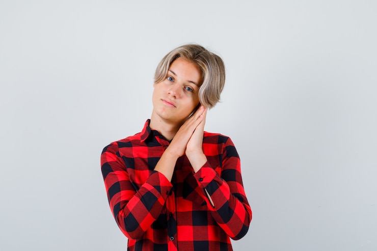 Foto grátis retrato de um lindo menino adolescente apoiado nas palmas das mãos como travesseiro em uma camisa quadriculada e com uma vista frontal sensata
