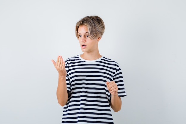 Retrato de um lindo menino adolescente olhando para a palma da mão em uma camiseta listrada e olhando chocado para a frente