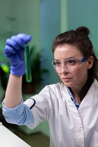 Foto grátis retrato de um médico bioquímico olhando para um tubo de ensaio médico com solução de dna verde