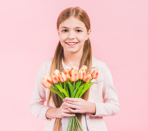 Retrato, de, um, menina feliz, olhar câmera, segurando, buquê tulipas, em, mão, ficar, contra, fundo cor-de-rosa