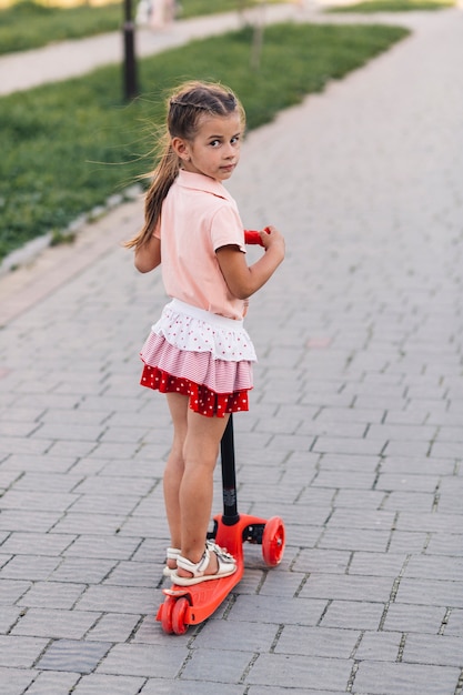 Retrato, de, um, menina, ficar, ligado, vermelho, empurrar scooter, olhando câmera