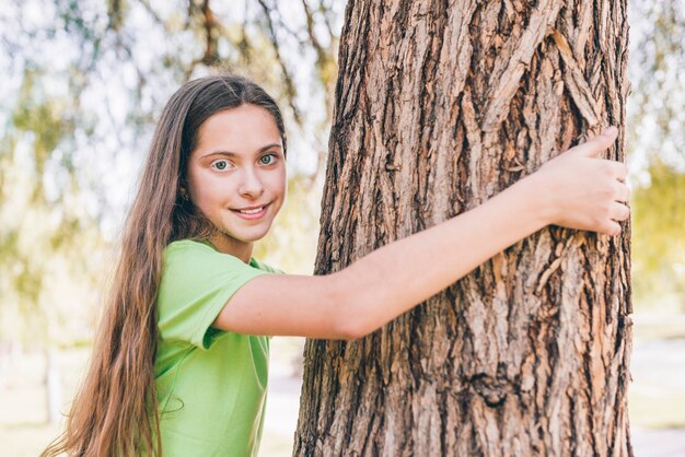 Retrato, de, um, menina sorridente, abraçar, tronco árvore