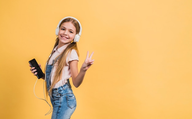 Foto grátis retrato, de, um, menina sorridente, escutar música, ligado, branca, headphone, gesticule, contra, amarela, fundo