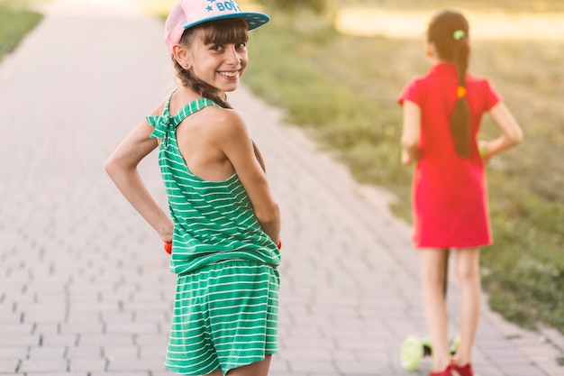 Foto grátis retrato, de, um, menina sorridente, ficar, ligado, empurrar scooter, olhando para trás