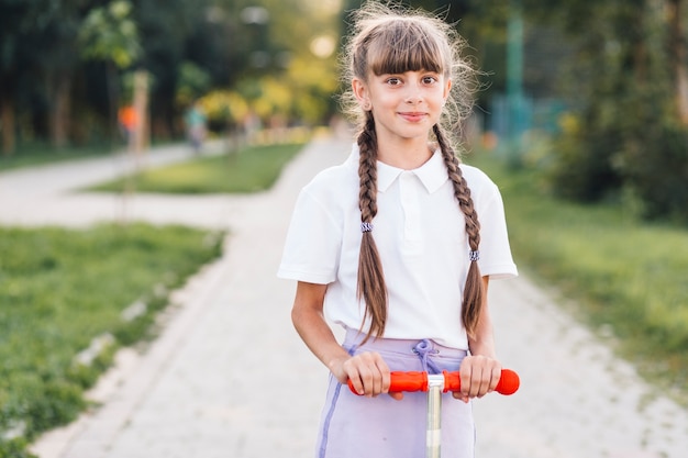 Retrato, de, um, menina sorridente, ligado, empurre scooter, parque