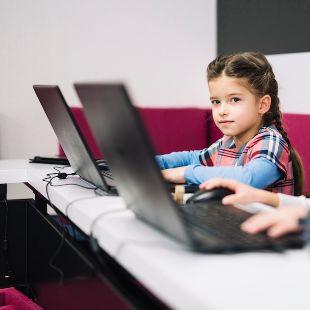 Retrato, de, um, menininha, olhando câmera, sentando, com, laptop, em, a, sala aula