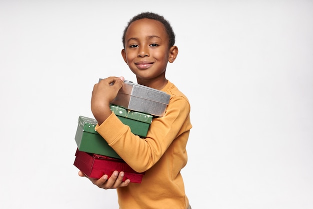 Foto grátis retrato de um menino africano alegre carregando caixas, recebendo presentes, olhando para frente com um sorriso alegre e feliz