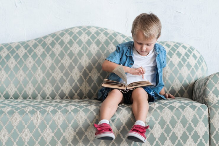Foto grátis retrato, de, um, menino sentando, ligado, sofá, apontar dedo, sobre, livro