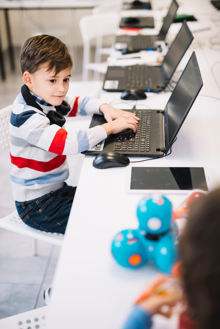 Foto grátis retrato, de, um, menino, usando computador portátil, olhar, criança, tocando, com, brinquedo, em, a, classe