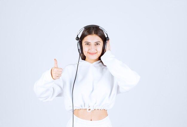 Foto grátis retrato de um modelo de garota jovem e bonito com fones de ouvido aparecendo um polegar.