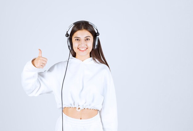 Retrato de um modelo de garota jovem e bonito com fones de ouvido aparecendo um polegar.