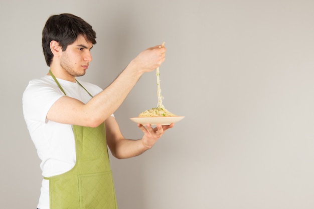 Retrato de um modelo de homem bonito no avental, segurando um prato com comida.