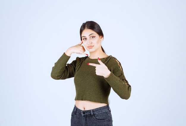 Retrato de um modelo de mulher jovem e bonita fazendo um sinal de chamada de telefone e apontando para o lado com o dedo indicador.