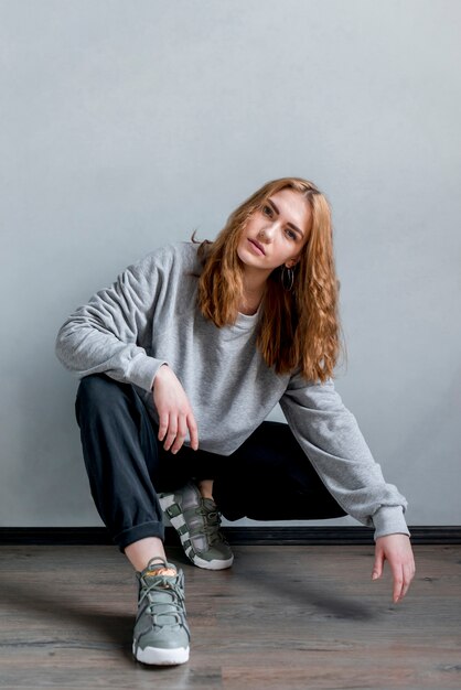 Retrato, de, um, mulher jovem, crouching, ligado, assoalho hardwood, contra, parede cinza