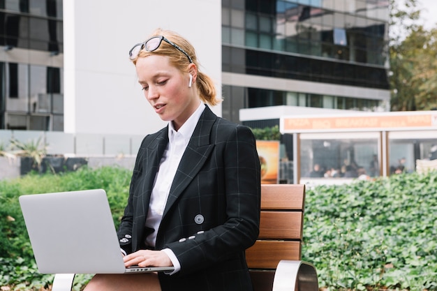 Retrato, de, um, mulher jovem, sentando, exterior, a, escritório, usando computador portátil