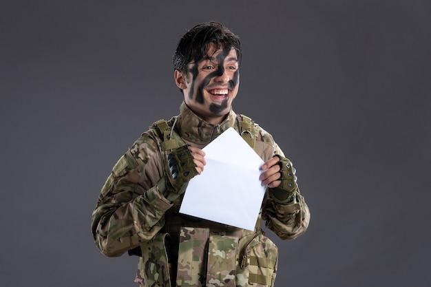 Retrato de um soldado camuflado feliz com a carta da parede escura da família