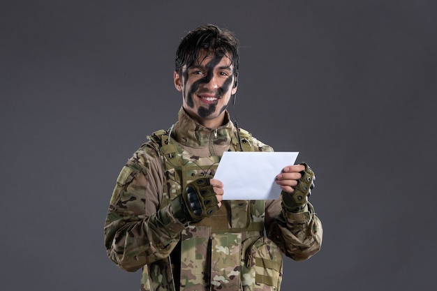 Retrato de um soldado camuflado lendo uma carta da família na parede escura