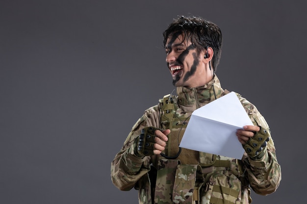 Retrato de um soldado camuflado segurando uma carta na parede escura