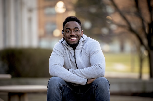 Retrato de um sorridente afro-americano sentado em um parque sob a luz do sol