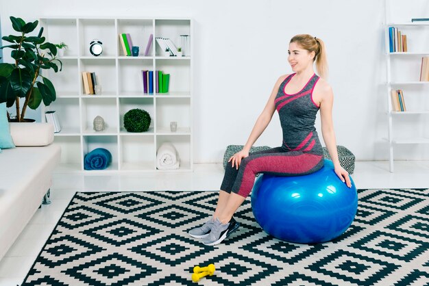 Retrato, de, um, sorrindo, condicão física, mulher jovem, sentando, ligado, azul, pilates, bola, olhando